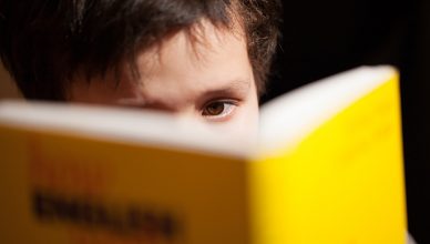 Young boy concentrating on reading a book with just his eyes visible over the top as he studies for class