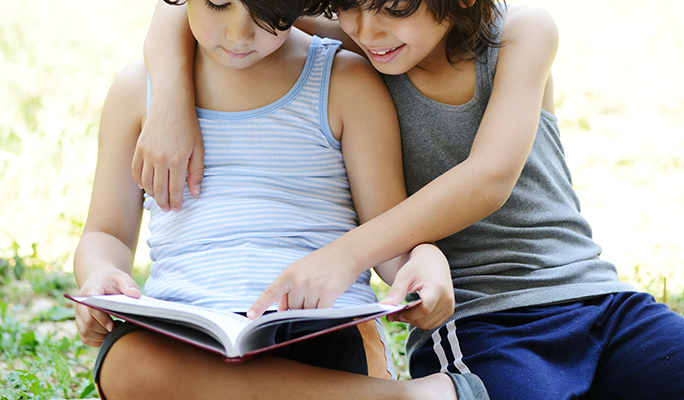 Little two boys reading a book in garden